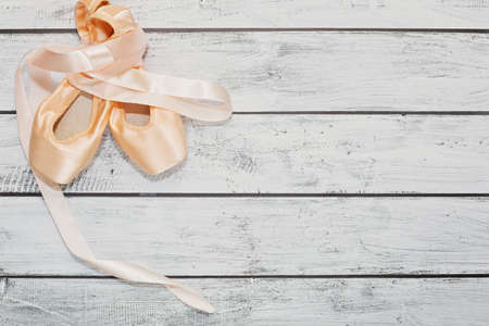 Traditional ballet new shoes - pointe - with silk ribbons crossed on the wooden stage background made of rough finished plank boards. Place for text, top view.の写真素材