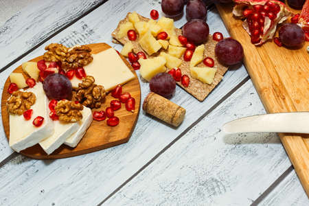 Refined red wine snack in european style - plenty varieties of cheese with fresh fruits. walnuts and rye crackers served on wooden table. European cuisine style. Close-up capture, selective focus.の写真素材