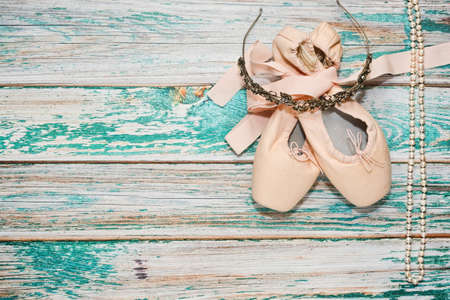 Classic ballet shoes with ribbons lie on wooden surface - theater stage - and some ballet show props - diadem with rhinestones and pearl necklace. Ballet practice or training concept. Top view.の写真素材
