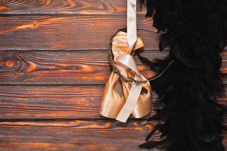 Pair of new ballet dancing shoes with hard insoles hand nearby black feather boa on the wooden background. Ready to dancing show concept. Place for text.の写真素材