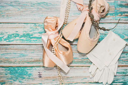 Two pairs of ballet shoes - glance and matt - and some scenic show props such as necklace and diadem - ready to perfomance on wooden stage with traces of old paint. Top view.の写真素材