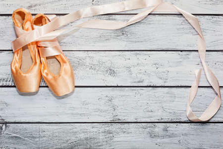 Pair of new silk ballet shoes with ribbons on the rough painted wooden background. Ballet dance practice and training concept. Top view, place for text.の写真素材