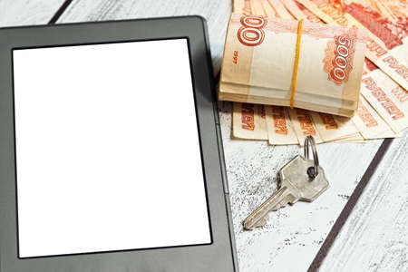 Business or residental properties rent or purchase via mobile app concept - stack of russian national currency - rubles - and a door key lie near diital tablet with a copyspace on blank screen.の写真素材