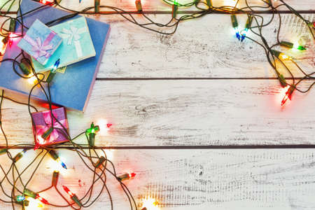 Christmas presents in tiny gift boxes collected on the rough painted wooden table in retro style and traditional New Year colorful garland. Winter holidays concept. Top view, place for text.の写真素材