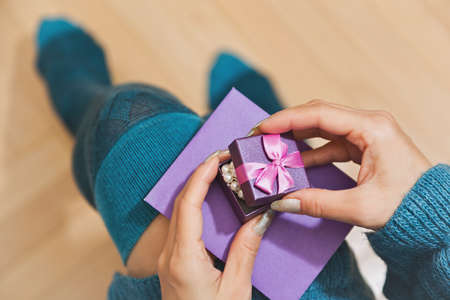 Young female person in blue dress and stockings unpacking a gift holding it on her knees with a envelope. Birthday, new year or christmas surprise present concept. First person view, selective focus.の写真素材