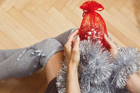 Teenage girl in high school socks with Christmas or New Year gift in pouch and tinsel garland. Traditional winter holidays concept. First person view or overhead capture, selective focus.の写真素材