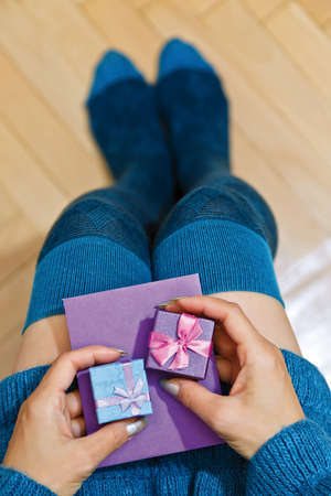 Young adult female person in blue dress and knee height warmer socks holding gifts in boxes and a congratulation card in envelope on her knees. Saint Valentine or Birthday idea. First person top view.の写真素材