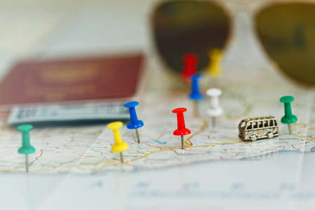 Road map with many places of interest highlighted by colored pins and a tiny toy bus. Some travel accessories on the background. Travel planning concept. Close-up capture, selective focus.の写真素材