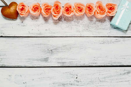 Rose blossoms, gift in handmade tiny box and wooden heart pendant on white rough finished wooden background made of planks in loft or rural style. Valentine Day concept. Top view, place for text.の写真素材