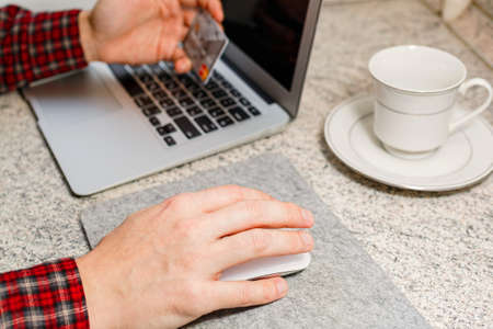 Man in checkered shirt ready for making an one touch online payment with a credit card and a laptop....