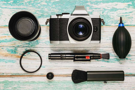 Vintage style camera and lens with cleaning kit - air pump, cleaning pen, brush and lens protective filter on rough painted wooden background. Taking care of photographer equipment concept. Top view.の写真素材