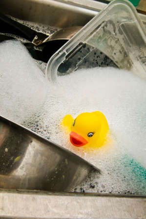 Rubber duck in a sink with dirty dishesの写真素材
