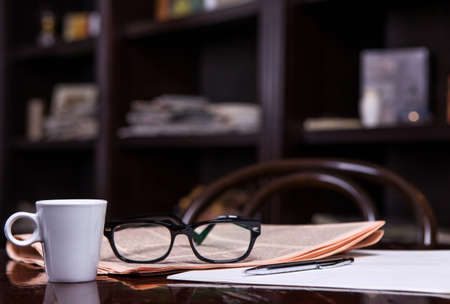 Newspapers and coffee cup, reading glasses, pen and striped paper.の写真素材