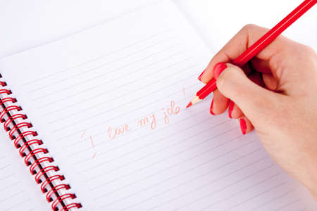 Woman writing with wooden pencil on white sheet, I love my jobの写真素材