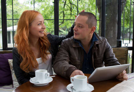 Two students drinking coffee and having fun with tablet In cafeteria