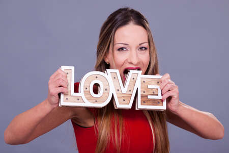 Valentines Day. Woman wearing red dress holding sign love symbol on grey backgroundの写真素材
