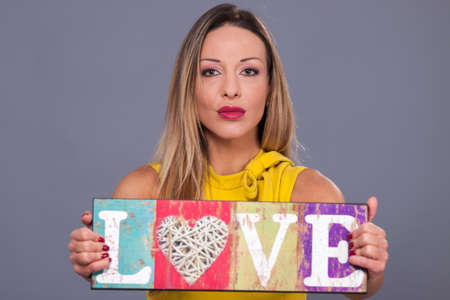 Valentines Day. Woman wearing yellow dress holding sign love symbol on grey backgroundの写真素材