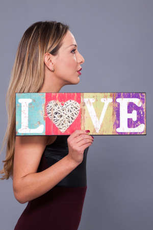 Valentines Day. Woman wearing red dress holding sign love symbol on grey backgroundの写真素材