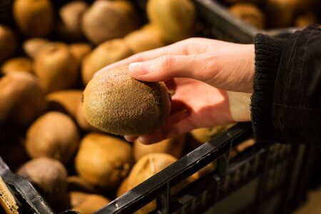 Womans hand holding kiwi on a lot of blurred kiwi in basket background.の写真素材