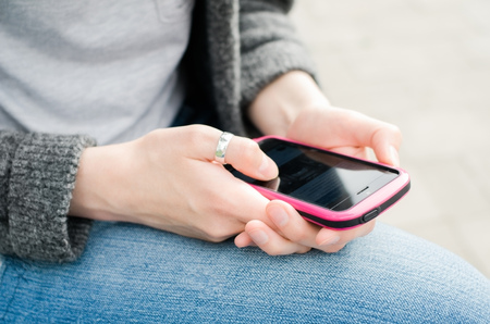 Beautiful young hipster woman using smart phone on a gray background. Close up shot.