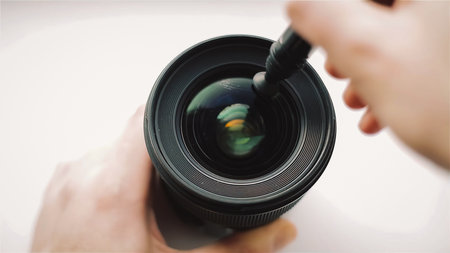 Beginning photographer or video cameraman is carefully cleaning the front glass of the lens with a professional cleaning pen for optics. Closeup shot.の写真素材