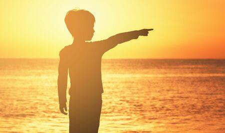 contour of a boy at sunrise sunset on the seashore of the ocean orange sky sea ocean boy shows his finger to the sideの写真素材