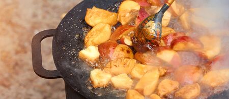 Fried apples in a cast-iron black frying pan on nature with wood spoon with Russian ornamentの写真素材