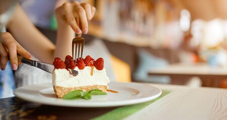 Womans hands holding a plate with slice of strawberry cheesecake. Girl hands cut the cake by fork.