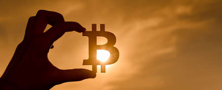 Bitcoin symbol in hand at sunset. sun through the signの写真素材