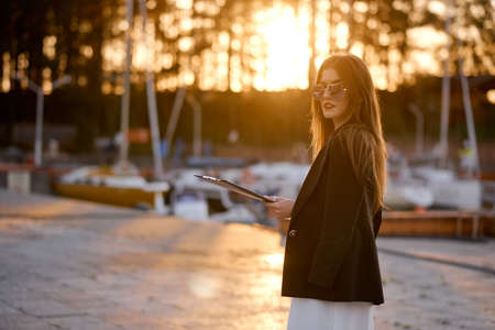 Business woman at sunset in jacket with folder on stone pier near yachtsの写真素材