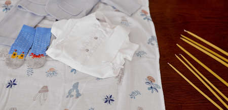 clothes for the baby on the diaper on a wooden table next to the candles of the christening . High...