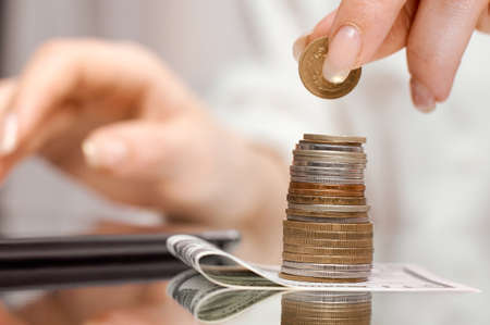 stack of coins on the banknote next to the tablet on which the girl counts her income . High quality...