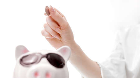 women's hand from top to bottom puts a coin in the piggy bank pig with glasses. High quality photoの写真素材