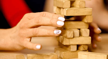 Woman pulls out one block of wooden game falling tower