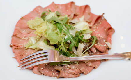 red meat snack with greens on a large white plate with a fork