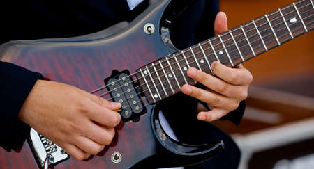 A man plays a modern electronic guitar. Hands on strings.