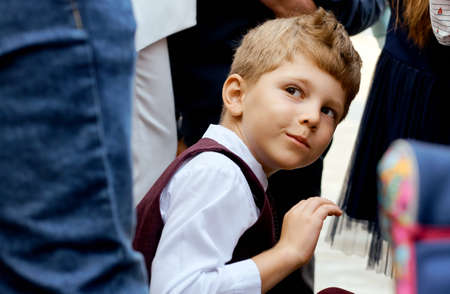 Boy in a strict suit peeps out from behind adults