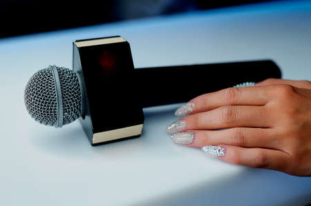 Microphone on a white table with an empty plate for the inscription next to the woman's hand. High...