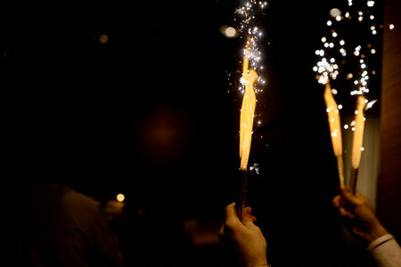 Hands Holding Sparkling Fireworks in Darkness.