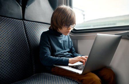 Focused Boy Typing on Laptop in Train.