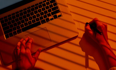 Female Hands Drawing on Paper beside Laptop with Dramatic Light.の写真素材