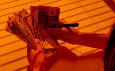Counting Mixed Currency Banknotes Under Warm Blinds Light.