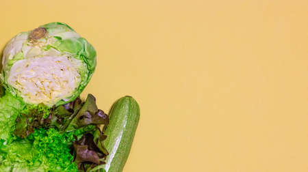 Still life of fresh, green vegetables. Zucchini, young cabbage, lettuce leaves. On yellow background. Located on the left. Space for text. Vertical photo. The view from the topの写真素材