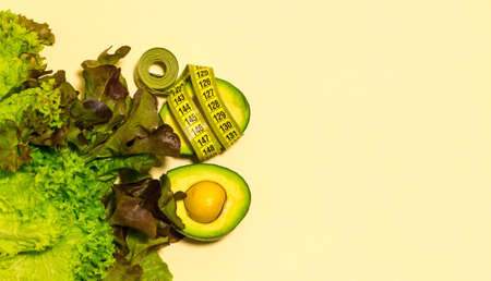 Banner. Still life of fresh, green vegetables. Avocado cut, lettuce leaves. Centimeter. On yellow background. Located on the left. Space for text. Vertical photo. The view from the top.の写真素材