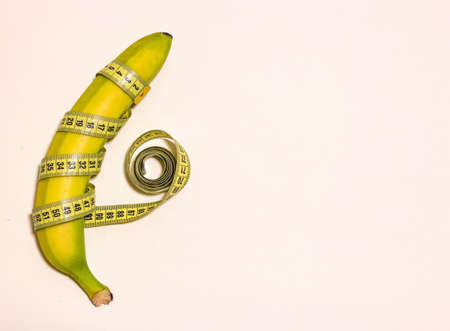 Yellow banana wrapped in a centimeter tape. Minimalism. Located on the left, on a pale pink background. The view from the top. Space for textの写真素材