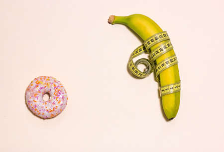 Pink doughnut and banana. Minimalism. Yellow banana wrapped in a centimeter tape. Located on the left, on a pale pink background. The view from the top. Space for textの写真素材