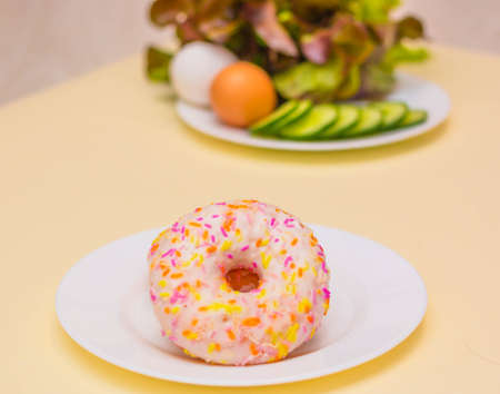 A donut or a salad. Salad on a plate. Chocolate donut. Health food. Dietary food. Choose between diet and junk food. Light background. The view from the top. Space for textの写真素材