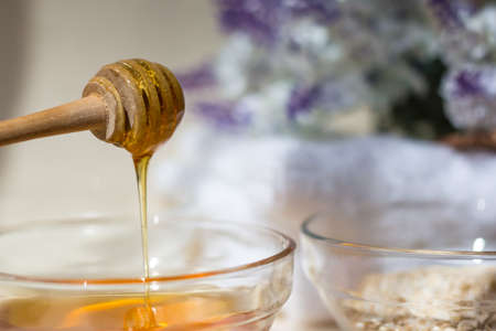 Home Spa skin care ingredients. Glass jars of oatmeal and yellow honey, a white towel for the...