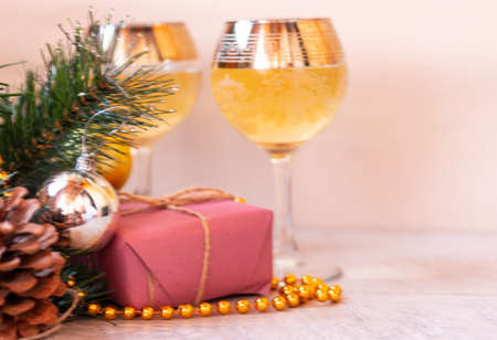 Two glasses of white wine on a light background. Gift box. Lighted candle. Decorations on a fir branch with a cone. Side view. Space for text. Soft image. Evening. Winter.の写真素材