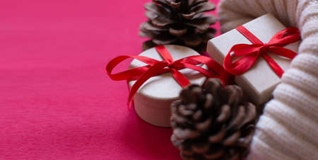 New years banner. Light, knitted sweater with cones and gift boxes tied with a red ribbon on a red background. Side view. Space for text.の写真素材